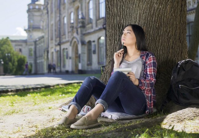 Exchange student sitting under tree, holding notebook, thinking on project, stock footage